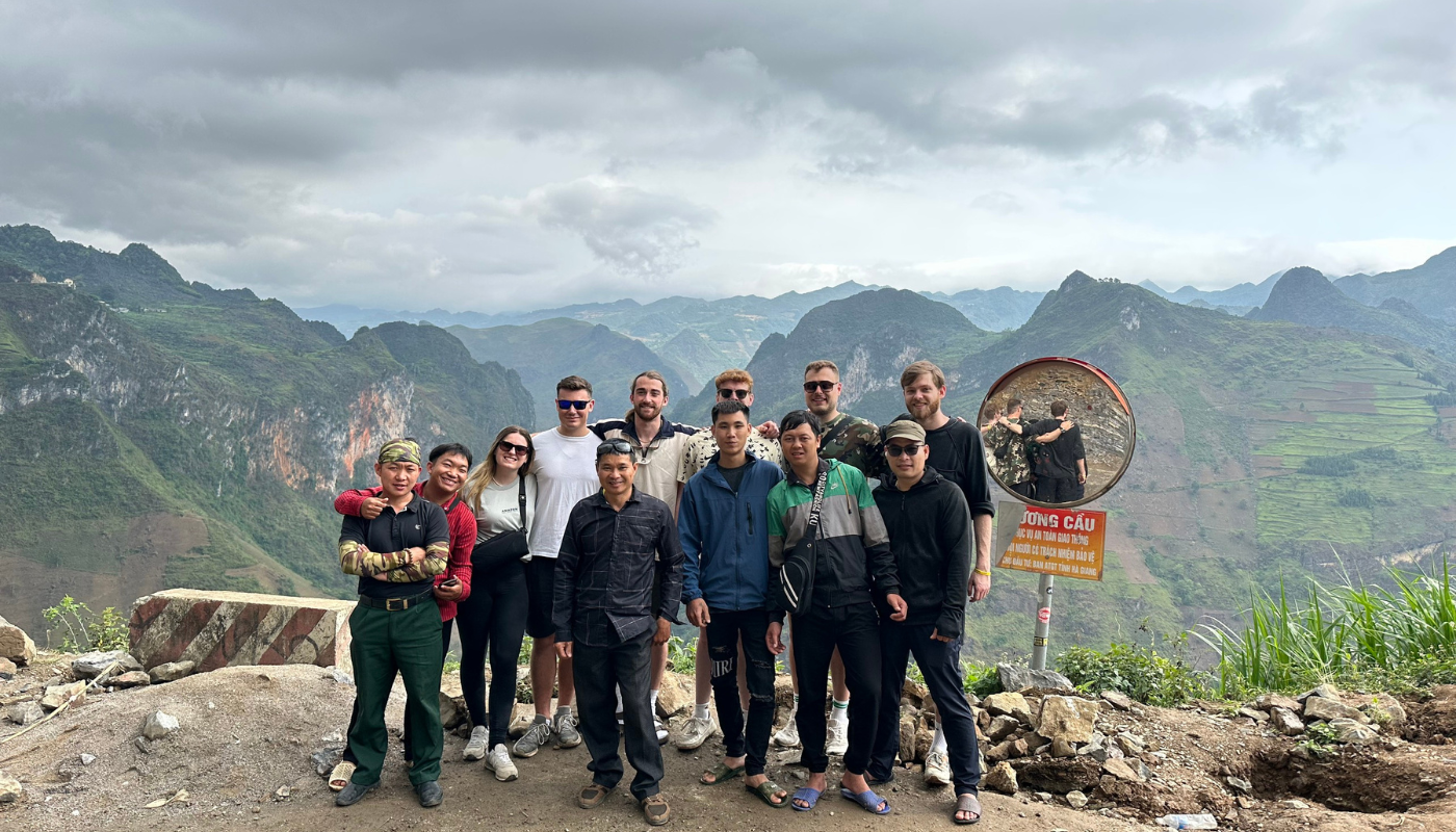 Group of tourists and local taking a photo at Ma Pi Leng Pass with a panoramic view of majestic mountains in Hà Giang.